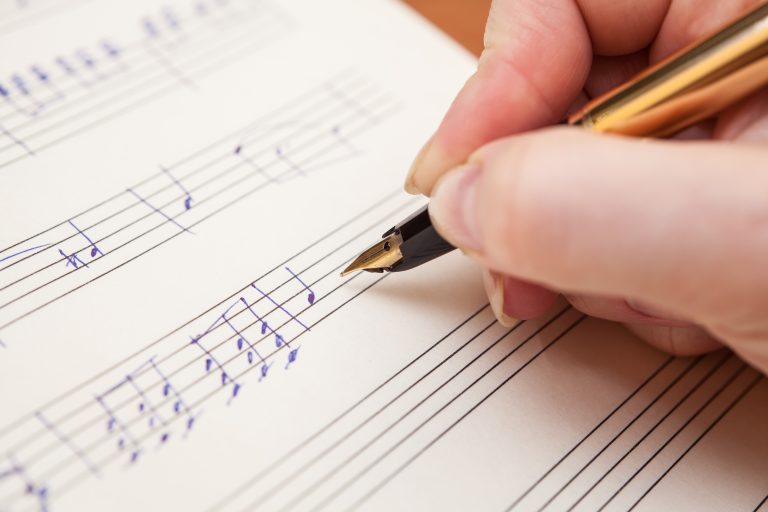 persona escribiendo notas musicales en partitura